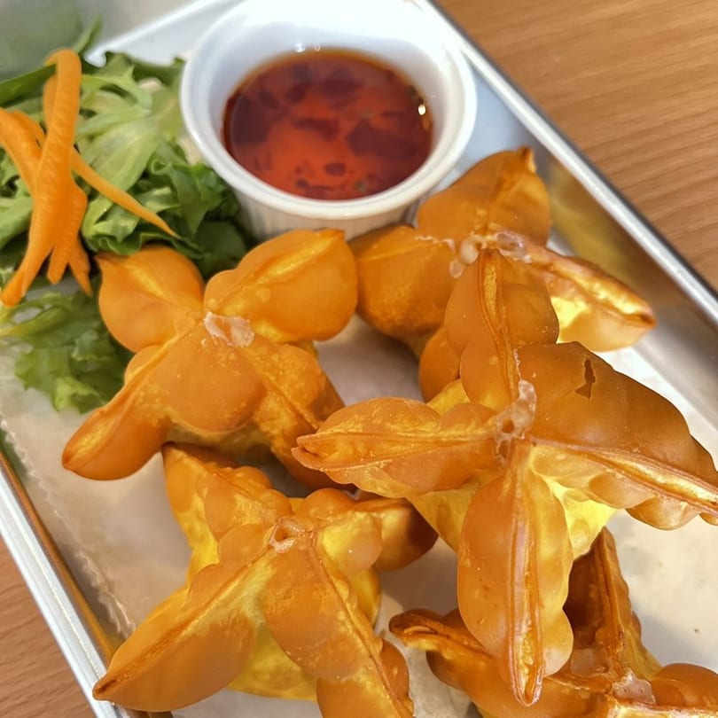 Golden-fried crab rangoons with a side of sweet chili sauce and lettuce on a metal tray.
